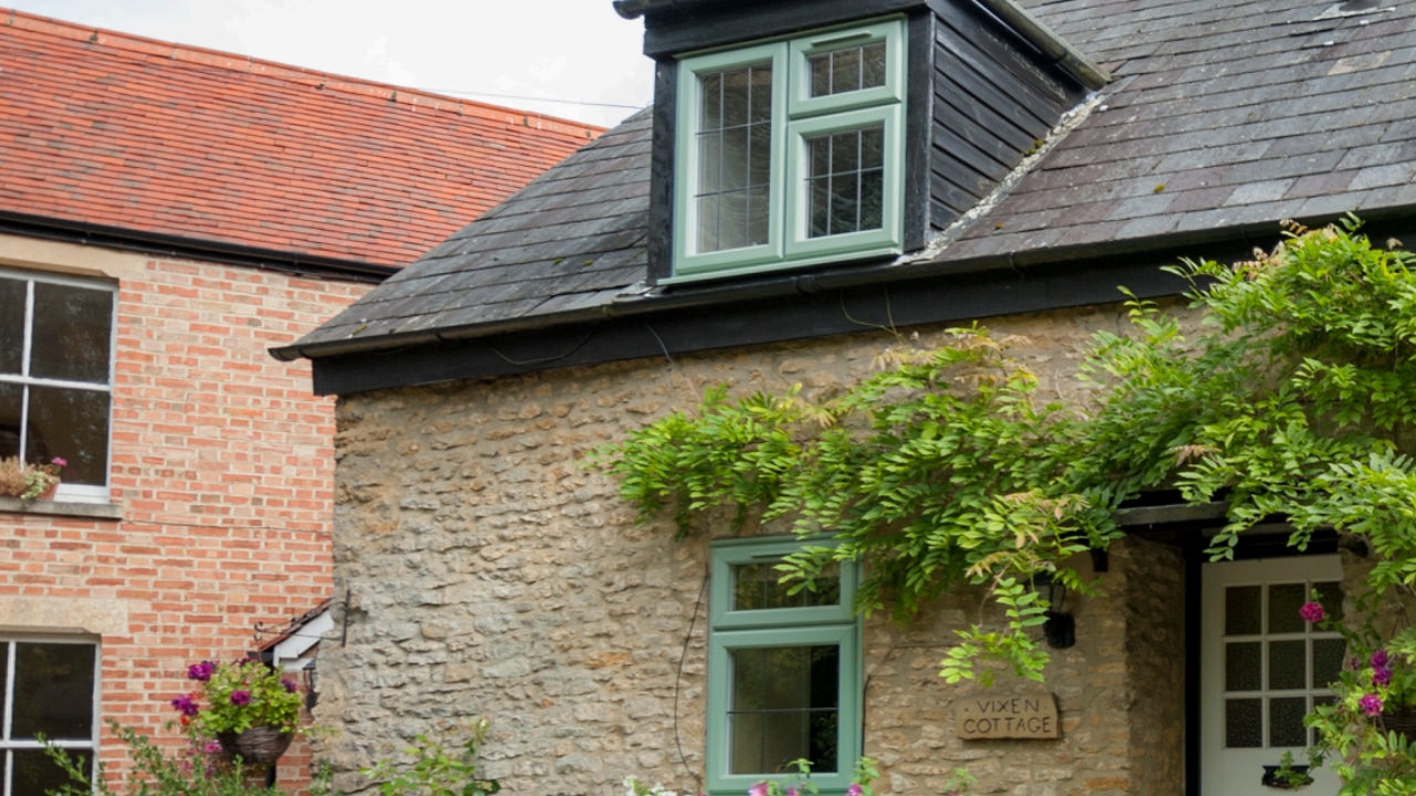 uPVC windows in Chartwell green installed in a traditional stone cottage with a dark roof.