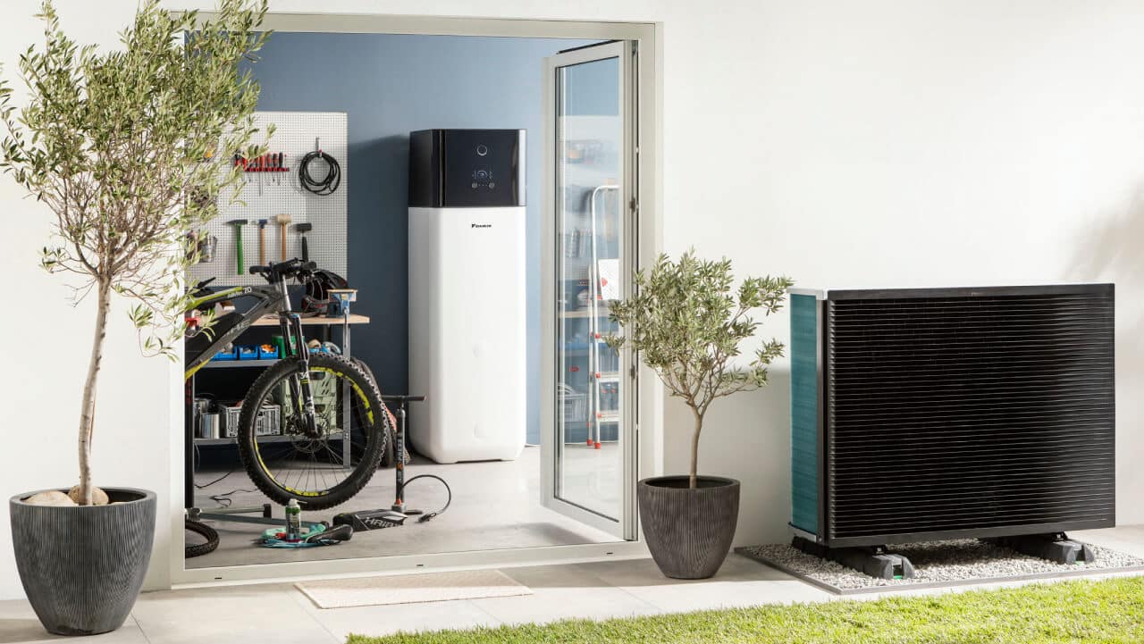A floor-standing Daikin Altherma 3 air source heat pump inside a utility room with an outdoor unit sitting in the garden of a house.