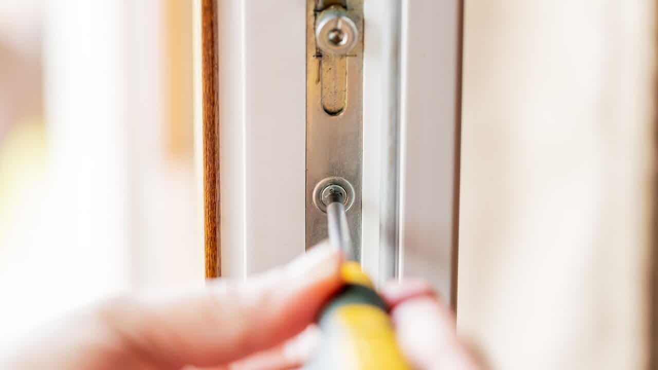 A person using screwdriver to repair a uPVC window lock.