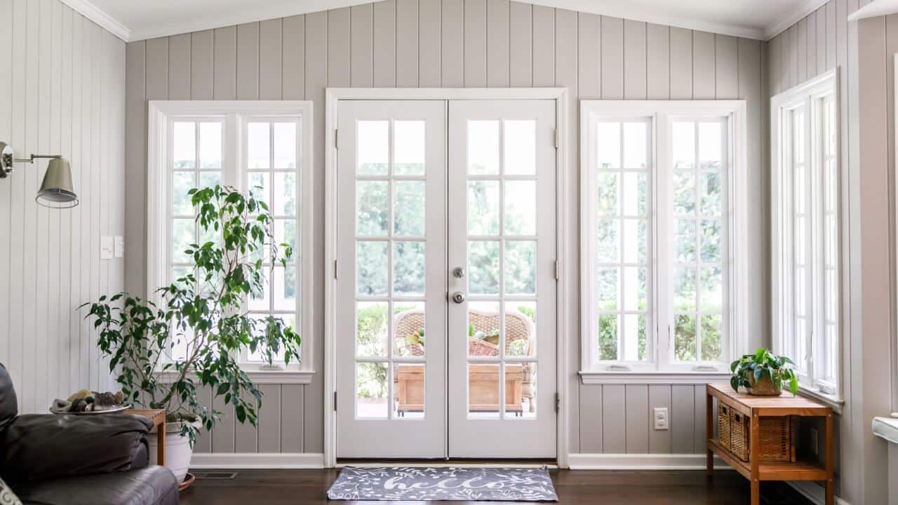 French doors and windows in white in a large, sunny room with a plant in front of one window.