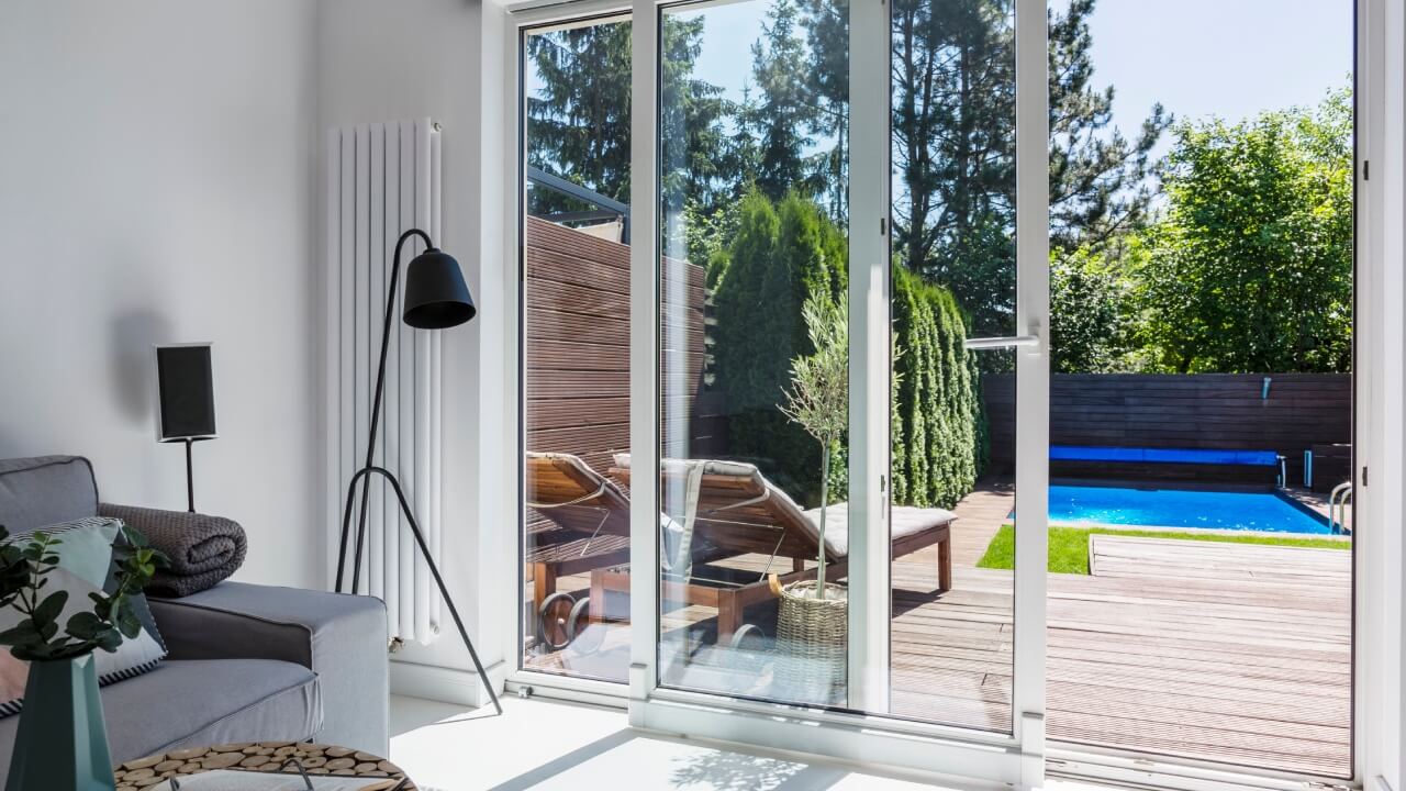 Doors and windows. A living room with a patio door leading to a wooden deck with a swimming pool in the background.