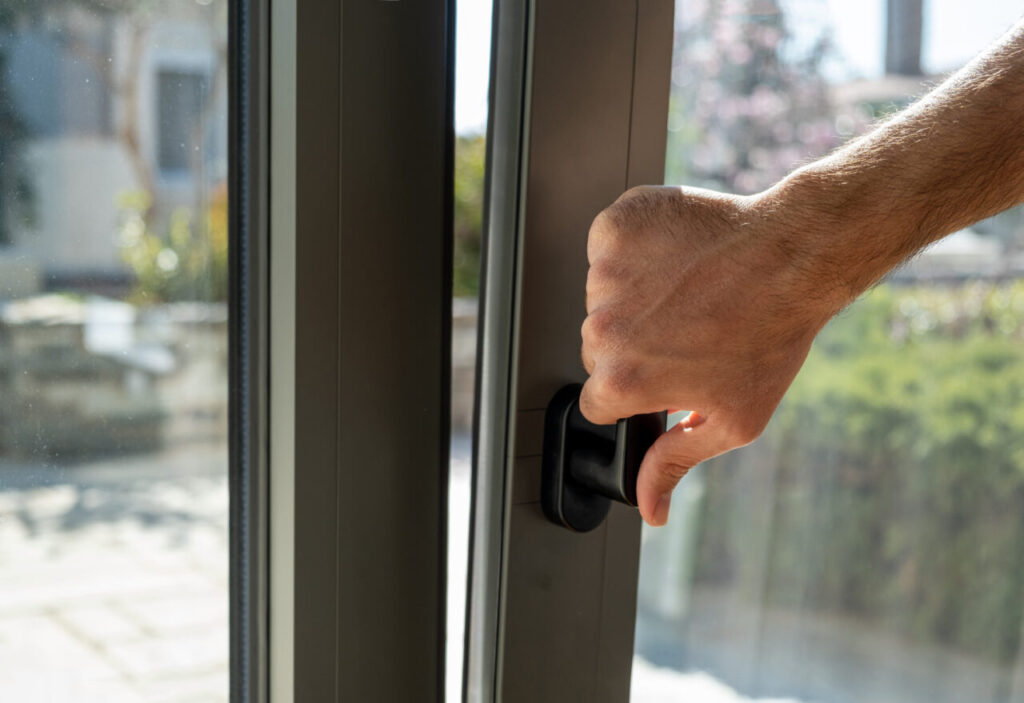 Tilt and turn grey color aluminum window, man holding the handle, fresh air for home. Male hand vertical open metal or PVC window, closeup view.